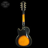 Back view of a vintage electric guitar with a black and orange color scheme on a black background.