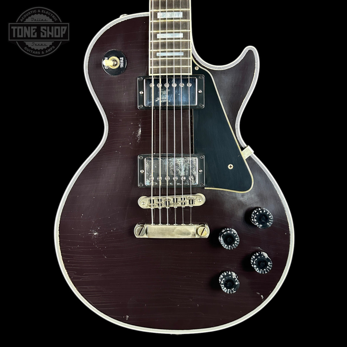 Electric guitar with a dark finish on a black background, featuring the 'Tone Shop' logo.
