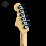 Close-up of a guitar headstock with a natural maple wood finish and six black tuning pegs featuring light blue circular inserts, shown against a solid black background.