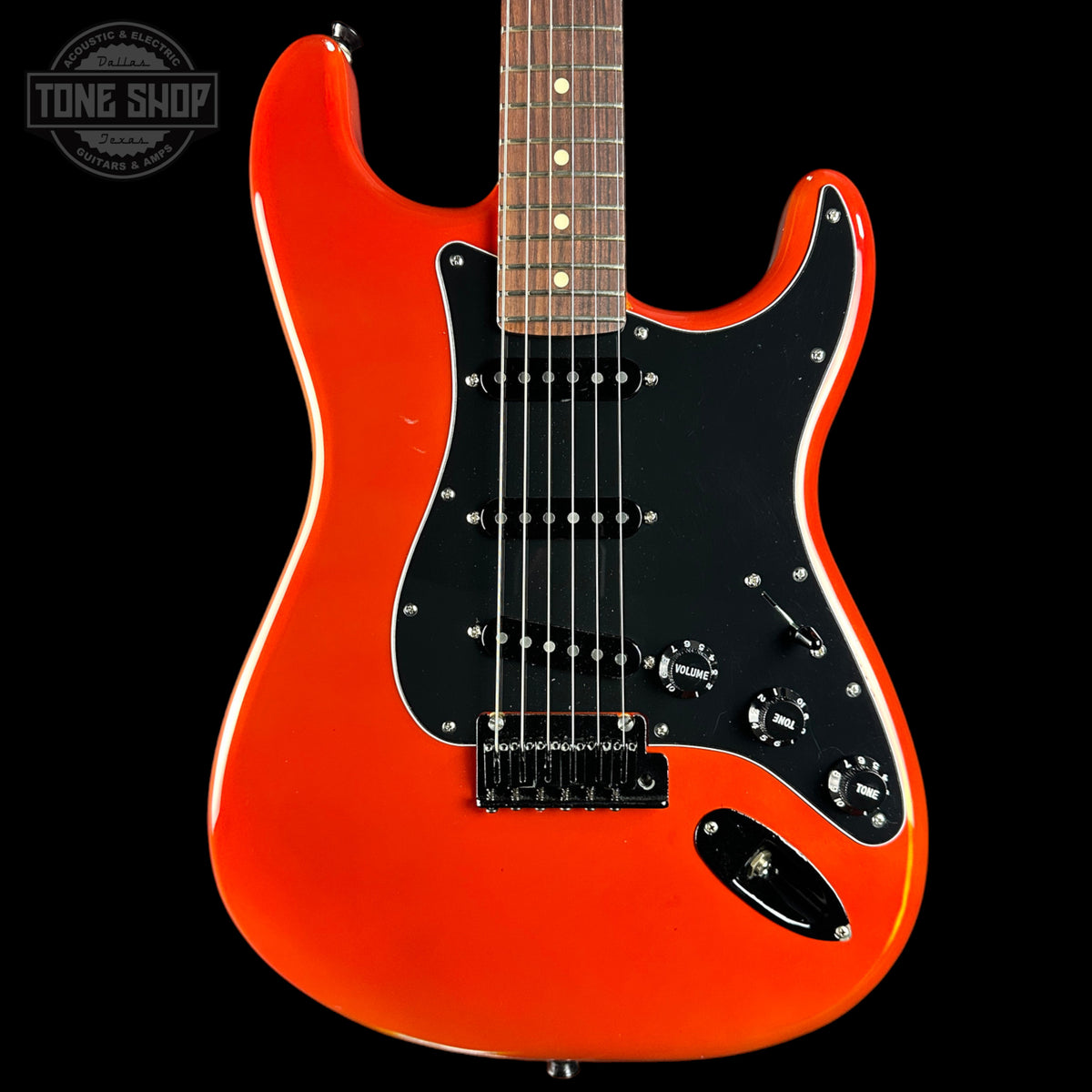 A classic electric guitar with a vibrant orange body, black pickguard, and maple fretboard, shown against a solid black background with a Tone Shop watermark in the top left corner.