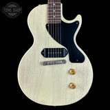 White electric guitar with a black pickguard on a black background, featuring the Tone Shop logo.