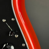 Close-up detail of an electric guitar body showing a glossy red maple neck curving over a black pickguard with silver screws and hardware.