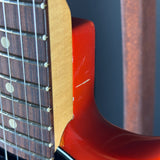 Close-up detail of an electric guitar showing the red body edge, maple fingerboard, and dark fretboard with white dot inlays.