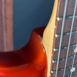 Close-up detail of an electric guitar showing the glossy red-orange body edge, the natural wood neck, and the strings against a dark blue background.