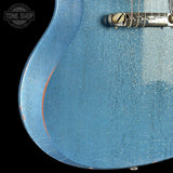 Close-up of a blue electric guitar with a 'Tone Shop' logo in the corner.