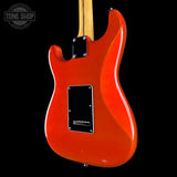 A close-up of the back of a glossy orange electric guitar body, showing a black pickguard, silver hardware, and part of a light wood neck against a black background. A Tone Shop watermark is visible in the upper left corner.