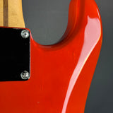 Close-up of a glossy red electric guitar body with a black pickguard and part of the light wood neck visible against a dark gray background.