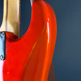 Close-up of a glossy red electric guitar body with a light wood neck and dark blue-gray background.
