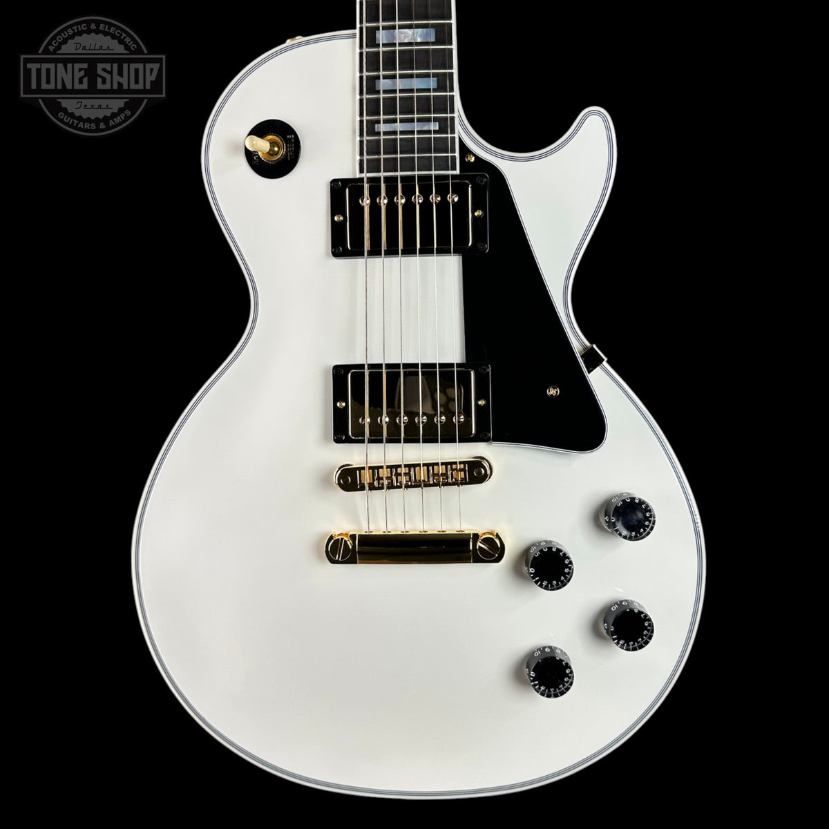 White electric guitar with a black pickguard on a black background, featuring the 'Tone Shop' logo.