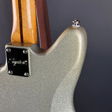 Close-up of the rear body of an electric guitar showing a glittery silver-gray finish, a black plate with silver hardware, and part of the wooden neck with a double stripe.