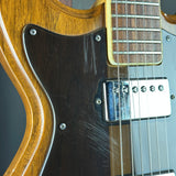 Close-up of a double-cutaway electric guitar showing the dark brown pickguard with visible scratches, the silver humbucker pickups, and part of the sunburst wood body.