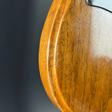 Close-up detail of a glossy wood guitar body corner showing the wood grain and finish against a dark gray background.