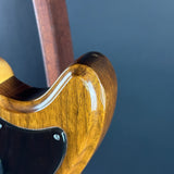Close-up of a glossy brown wooden electric guitar body with a black pickguard and a dark blue background.
