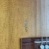 Close-up of a wooden surface with 'BAM' branding and a necklace.