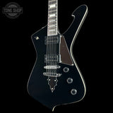 A black electric guitar with chrome hardware and a dark pickguard, shown against a solid black background with a Tone Shop watermark in the top-left corner.