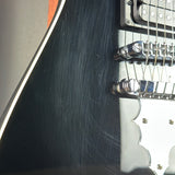 Close-up of a black electric guitar body with a chrome bridge and part of the white pickguard.