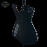 The back of a black electric guitar body with visible scratches and a clear protective cover over the pickguard, shown against a black background with a Tone Shop watermark in the top left.