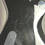 Close-up of a black guitar body with visible scratches, dust, and hair on the glossy surface, alongside part of a white pickguard and silver hardware.