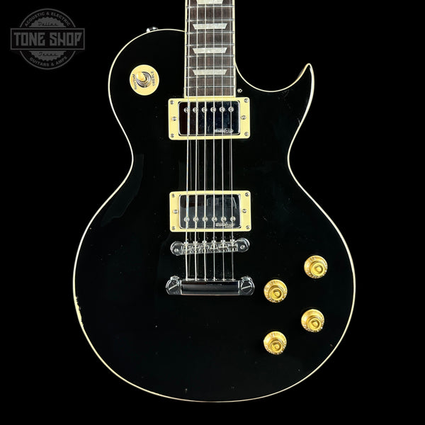 A black electric guitar with gold hardware and trim, shown from the front against a black background. A Tone Shop watermark is visible in the top-left corner.