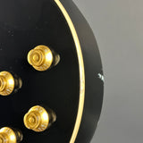 Close-up of a black electric guitar body showing gold-toned control knobs and a gold trim line against a gray background.