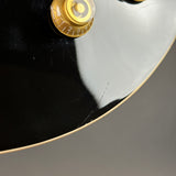 Close-up detail of a glossy black guitar body with a gold-toned control knob and a thin cream edge trim, photographed against a neutral gray background.