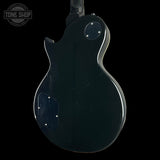 The back view of a black electric guitar against a solid black background, featuring a glossy finish with some visible wear and scratches. A circular 'TONE SHOP' watermark is visible in the top-left corner.