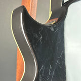 Close-up of the side of a black electric guitar body with visible scratches on the glossy finish, a thin gold edge stripe, and part of the wooden neck behind it.