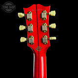 Close-up rear view of a red electric guitar headstock with six cream tuning pegs and gold hardware, shown against a black background. A Tone Shop watermark is visible in the upper left corner.
