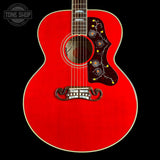 A red acoustic guitar shown from the front against a black background, featuring a decorative dark pickguard with yellow and blue floral details, a white bridge, and a white logo on the headstock partially visible at the top.