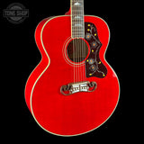 A red acoustic guitar with a cutaway body, featuring intricate floral inlays on the pickguard and a silver-toned bridge, shown against a solid black background.