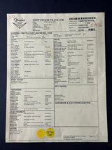 A printed Fender Shop Floor Traveler form sheet with handwritten notes and a yellow sticker, photographed on a dark blue background.