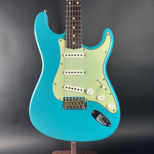 Blue electric guitar on a stand against a dark background