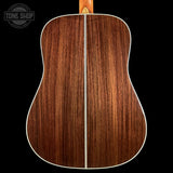Back view of a wooden acoustic guitar with a visible brand logo in the corner.