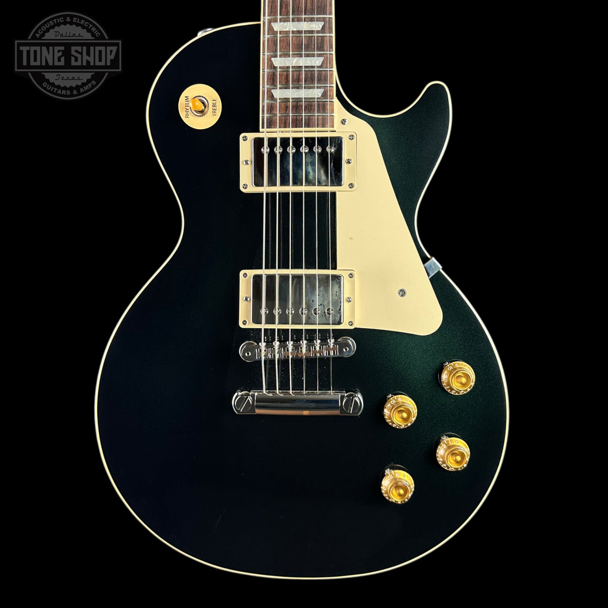 A black electric guitar with gold hardware and a cream pickguard, shown from the front against a black background. A Tone Shop watermark is visible in the top left corner.