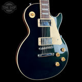 A black electric guitar with a cream pickguard and gold hardware, shown against a solid black background with a Tone Shop watermark in the top left corner.