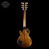 A classic electric guitar shown from the back, featuring a glossy brown wood finish, black pickguard, and gold tuning pegs, set against a solid black background with a Tone Shop logo in the top left corner.