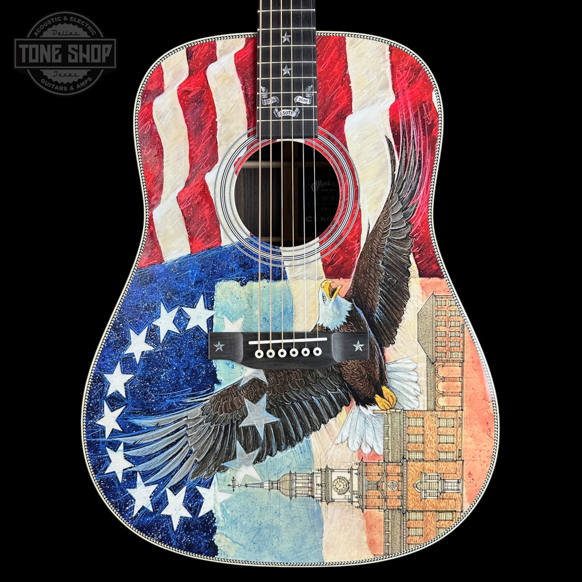 Acoustic guitar with a colorful design featuring an eagle, stars, and a building on a black background.