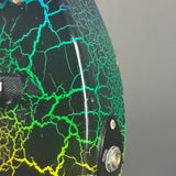 Close-up of a motorcycle helmet shell showing a glossy black base with a vibrant green and yellow crackle pattern, a clear visor, and a black chin bar.