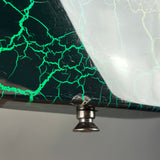 Close-up of a decorative tabletop or panel with a split design: one side is dark green with bright green veining, the other side is white with pale yellow veining, and a small metallic knob or hardware piece is visible at the bottom center.