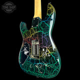 A custom electric guitar body with a black base and a vibrant, multicolor crackle pattern in green, blue, yellow, and purple. The guitar features white hand-written style signatures across the lower portion and is photographed against a solid black background.