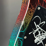Close-up of an electric guitar body showing a vibrant rainbow crackle finish that transitions from red and orange to yellow, green, and blue, with a black pickguard featuring a white signature.