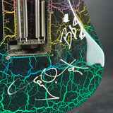 Close-up of a signed electric guitar body featuring a black base with vibrant green, blue, yellow, and pink crackle lightning patterns, signed in white marker.