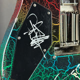 Close-up of an electric guitar body showing a black pickguard with a white scribble graphic, a black-and-red maple top edge, and a multicolor crackle pattern in green, blue, yellow, and red.