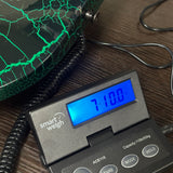 A close-up of a digital smart weigh scale displaying 710.0 on a blue screen, placed on a dark wood surface next to a green crackled decorative container.