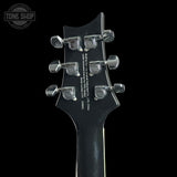Close-up of the headstock of a black electric guitar, showing six silver tuning pegs and white printed specifications on a black background. A Tone Shop watermark is visible in the top left corner.