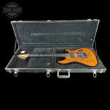 An electric guitar with a flame maple body in a vibrant orange-brown finish, displayed inside an open black hard case on a solid black background. A Tone Shop watermark is visible in the top-left corner.