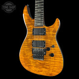A close-up of an electric guitar body with a vibrant orange and brown flamed maple wood finish, featuring black hardware and pickups, set against a solid black background.