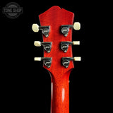 Close-up of the headstock of a red electric guitar against a black background, showing six black tuning pegs with cream-colored knobs and a glossy red finish. A Tone Shop watermark is visible in the top left corner.