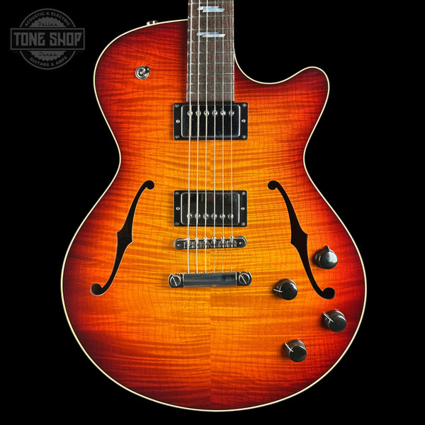 A double-cutaway electric guitar with a vibrant sunburst finish, featuring a natural wood grain pattern that transitions from bright orange to dark brown. The guitar is shown from the front against a solid black background, with a Tone Shop watermark in the upper left corner.