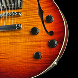 Close-up of a semi-hollow electric guitar body showing a sunburst finish that transitions from bright orange to dark brown, with black control knobs and a gold-toned binding edge against a black background.